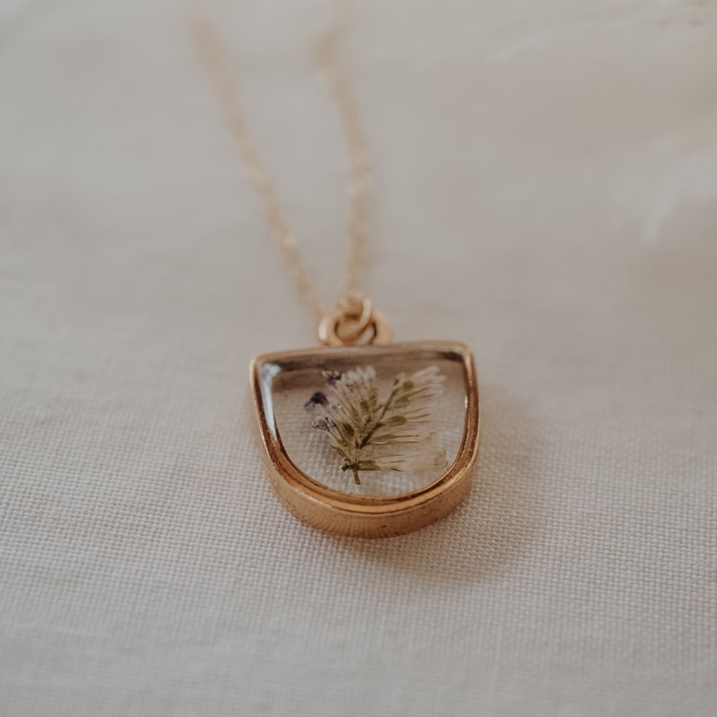 Caspia Botanical Necklace featuring real pressed Caspia flowers in cream and purple tones, set in resin within an antique gold plated half-oval bezel. 