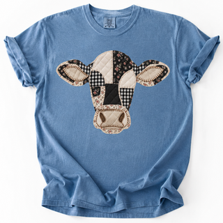 A light blue short-sleeve crewneck t-shirt featuring a cow head patchwork graphic on the front, laid flat against a white background.
