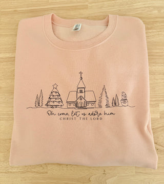 Folded pink sweatshirt with Christmas-themed design and text on a wooden surface