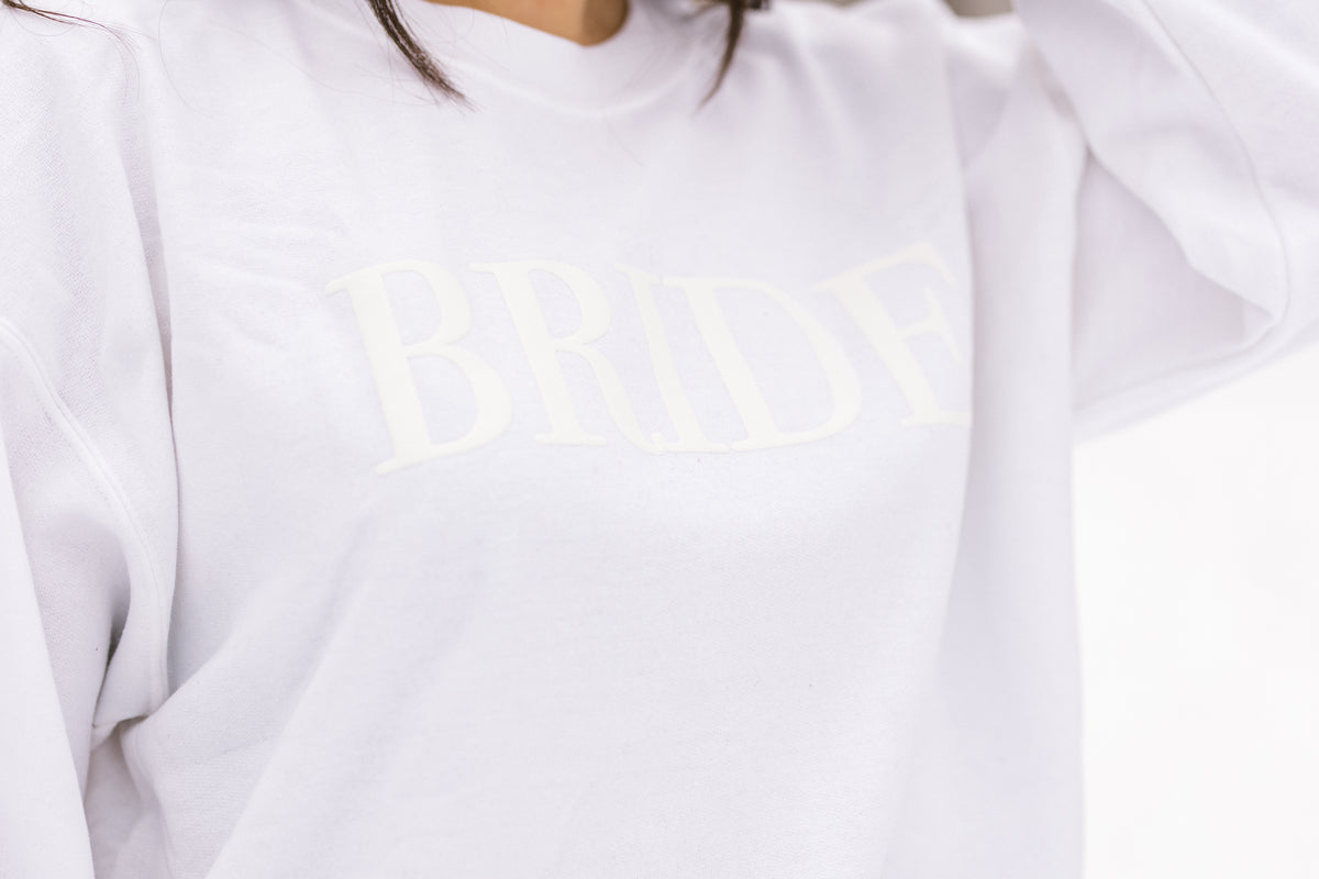 A women's crewneck sweatshirt with the word "Bride" elegantly embssed text on the front. This soft and comfortable white sweatshirt is perfect for the bride-to-be as she prepares for her big day. Available in unisex sizes Small to Extra Large, made from a preshrunk 50/50 cotton and polyester blend.