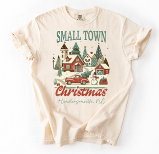 Beige t-shirt with Christmas-themed design featuring a small town scene on a white background.