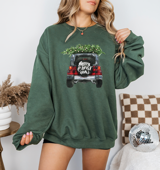 Green sweatshirt with Christmas truck design worn by a person, sitting on a couch.