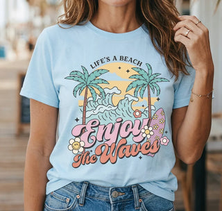 Person wearing a light blue t-shirt with 'Life's a Beach, Enjoy the Waves' design.