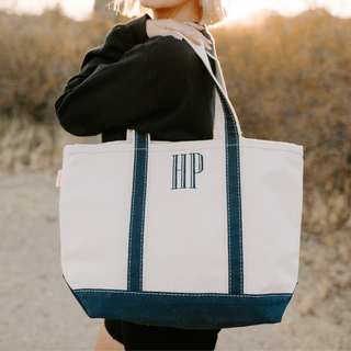 Woman holding a tote bag with initials, standing outdoors.