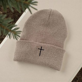 Gray knit beanie with a black cross on a light surface with greenery in the background