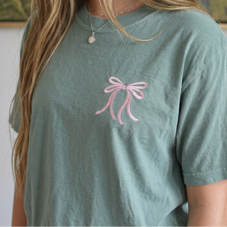 Green t-shirt with a pink bow design worn by a person.