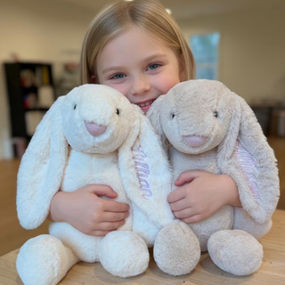 Child holding two plush bunny toys on a wooden surface