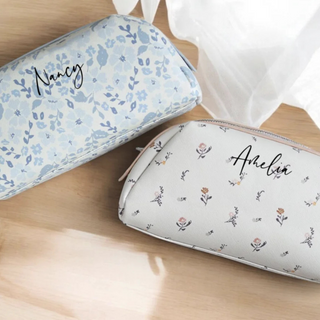 Two floral-patterned pouches with names 'Nancy' and 'Amelia' on a wooden surface.