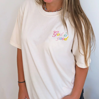 Person wearing a white t-shirt with 'God is good' text in colorful letters against a plain background