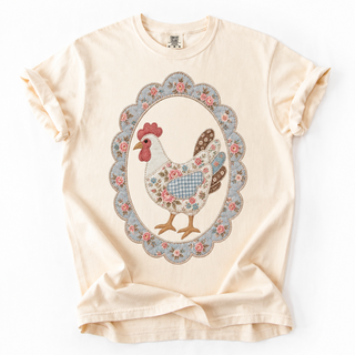 A cream-colored short-sleeve t-shirt with a ruffled collar and cuffs, featuring a central graphic of a patchwork-style chicken inside an oval floral frame.