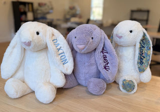 Three plush bunny toys with personalized names on a wooden surface.