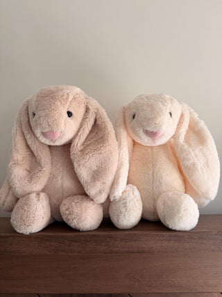 Two plush bunny toys sitting on a wooden surface with a neutral background