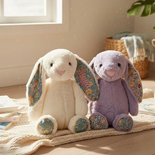 Two plush bunny toys, one white and one purple, with floral ear accents on a wooden floor.
