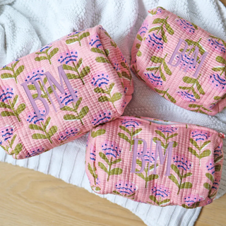 Three pink patterned pouches with initials on a white surface