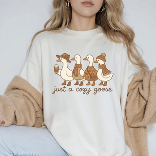 Person wearing a white sweater with a graphic of ducks and text 'just a cozy goose' on a plain background.