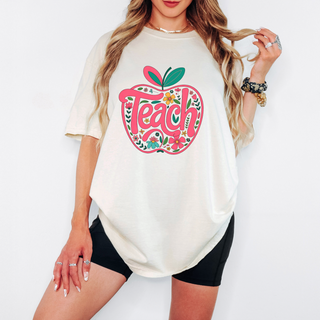 Boho teacher shirt with pink and floral apple graphic and the word Teach, modeled with casual summer outfit