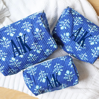Three blue pouches with floral patterns and initials on a white surface
