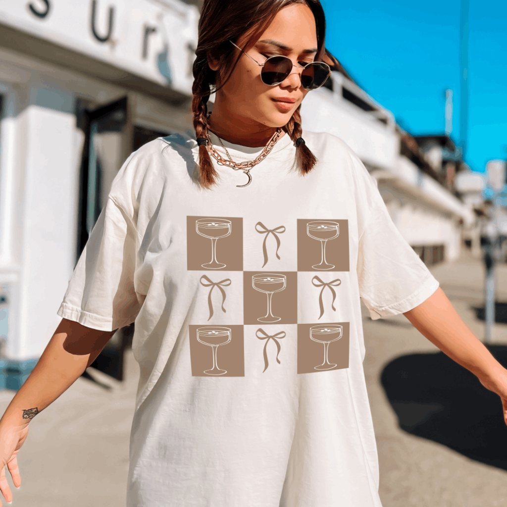 Embrace a blend of sophistication and playfulness with the Bow &amp; Espresso Martini Checkered Preppy Graphic Comfort Colors Tee from Melody Faye. This tee features a stylish checkered pattern adorned with a bow and an espresso martini graphic, capturing a chic, preppy aesthetic. Crafted from ultra-soft Comfort Colors fabric, it offers a relaxed fit and a lived-in feel, ensuring comfort throughout the day.​