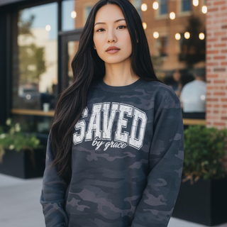 Woman wearing a camo sweatshirt with 'SAVED by grace' text outdoors.