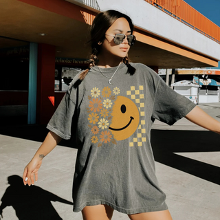 Woman wearing a gray t-shirt with a smiley face and floral design outdoors.