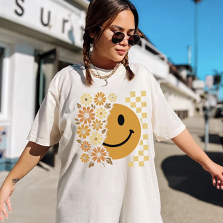Woman wearing a white t-shirt with a smiley face and floral design, standing on a street.