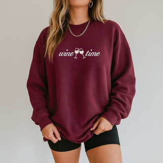 Maroon sweatshirt with 'wine time' text and wine glass graphics worn by a person on a plain background
