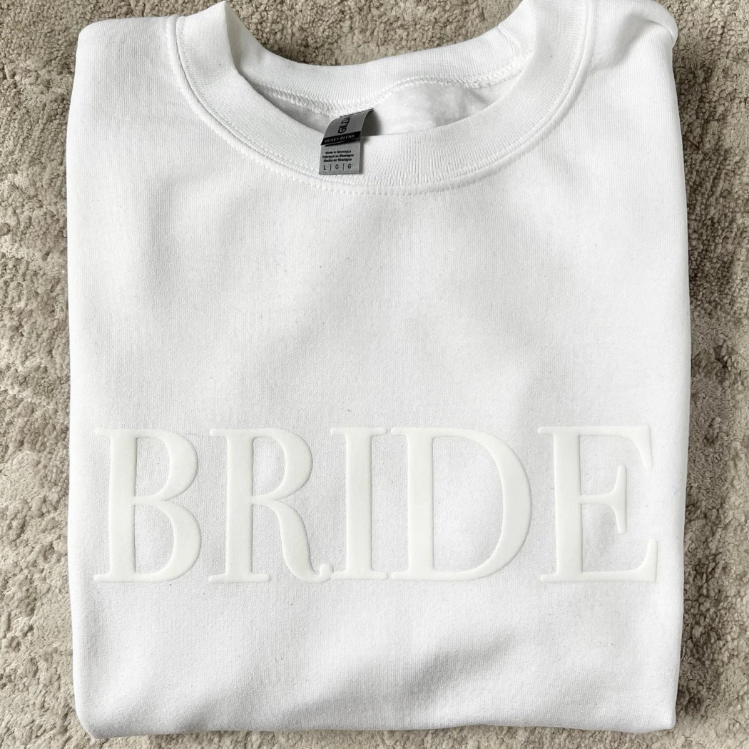 A women's crewneck sweatshirt with the word "Bride" elegantly embssed text on the front. This soft and comfortable white sweatshirt is perfect for the bride-to-be as she prepares for her big day. Available in unisex sizes Small to Extra Large, made from a preshrunk 50/50 cotton and polyester blend.